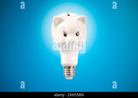 Lampadina a forma di salvadanaio in porcellana bianca, isolata su sfondo blu, messa a fuoco morbida in primo piano, Foto Stock