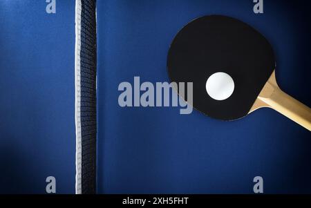 Paddle da ping pong e palla bianca su un tavolo blu con rete. Vista dall'alto. Foto Stock