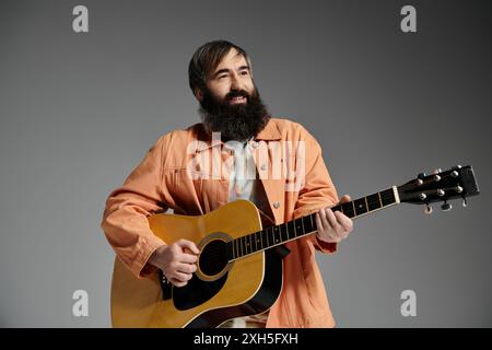 Un uomo con la barba suona una chitarra acustica in uno studio con uno sfondo grigio. Foto Stock