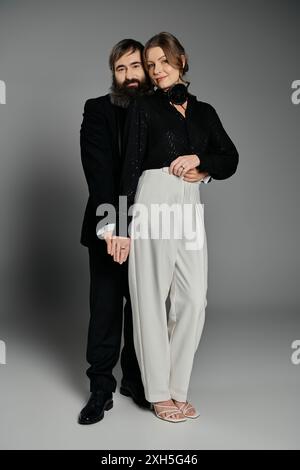 Una coppia elegante si posa in uno studio, l'uomo con la barba e la donna con pantaloni bianchi e top nero, creando un ritratto d'amore senza tempo. Foto Stock