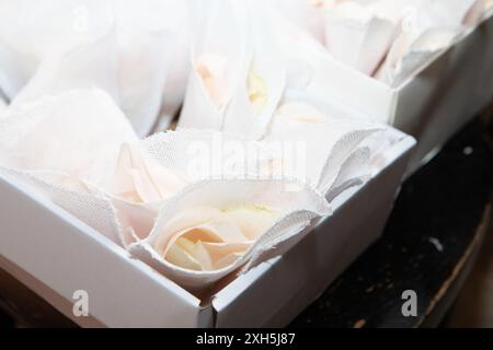 I delicati petali di rosa bianchi avvolti in tessuto bianco sono esposti in scatole bianche, pronte per essere consegnate come bomboniere agli ospiti Foto Stock