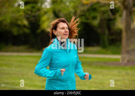 Donna anziana che indossa abbigliamento sportivo che corre nel parco godendosi la pensione attiva Foto Stock