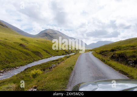 Un tranquillo fiume si snoda attraverso la lussureggiante e verdeggiante Glencoe Valley con torreggianti montagne sullo sfondo. Foto Stock