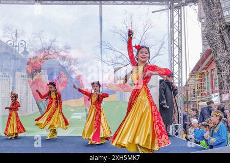 Almaty, Kazakistan - 21 marzo 2024: Ragazze asiatiche felici in abiti tradizionali e luminosi che ballano danza tagika durante la celebrazione delle vacanze primaverili Foto Stock