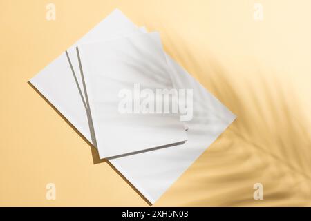 Una pila di carta bianca vuota su sfondo giallo con spazio per la copia. La luce del sole proietta ombre morbide, aggiungendo un tocco caldo e creativo alla setu minimalista Foto Stock