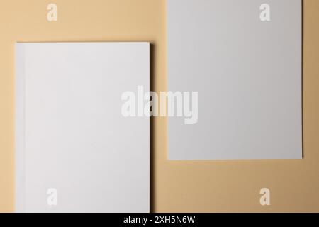 Due fogli bianchi vuoti su sfondo beige, con spazio di copia. Ideale per i mock-up di progettazione grafica o il posizionamento dei contenuti. Foto Stock