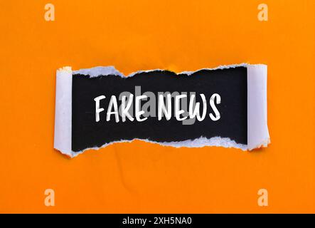 Falso messaggio scritto su carta arancione strappata con sfondo nero. Simbolo di notizie false concettuali. Copia spazio. Foto Stock