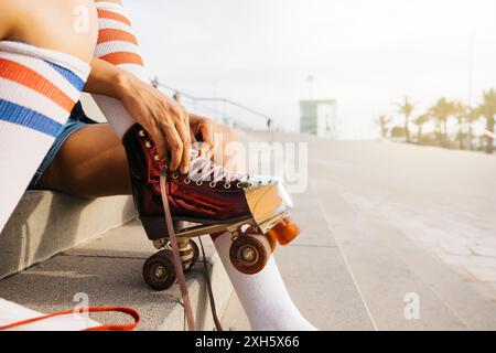 Primo piano di una giovane donna che stringe un paio, seduta su gradini, di pattini, preparandosi per una sessione di pattinaggio. Foto Stock