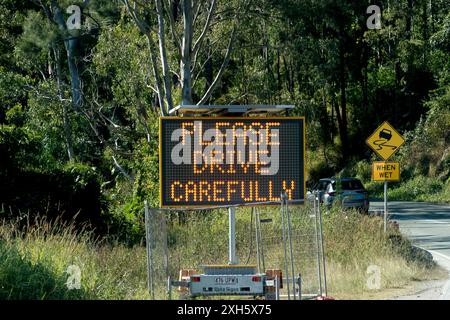 Educato cartello stradale illuminato "Please Drive carefully" accanto alla strada trafficata nel Queensland, Australia, nella verde area boschiva vicino a Gold Coast. Foto Stock