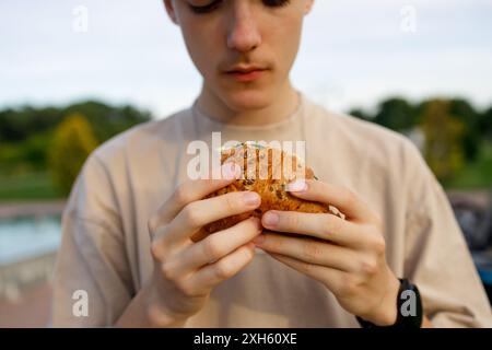 Selective focus on hands of young person eating sandwich outdoors Stock Photo