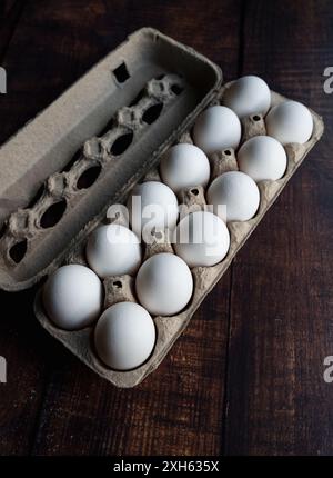 Close up angled view of carton of dozen white eggs on wood table. Stock Photo