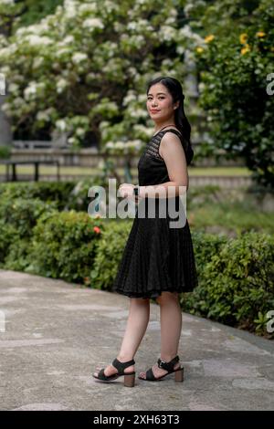 Asian lady with long black braided hair, wearing black dress outdoors Stock Photo