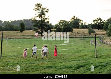 Children playing volleyball with a pink ball in a field at dusk Stock Photo