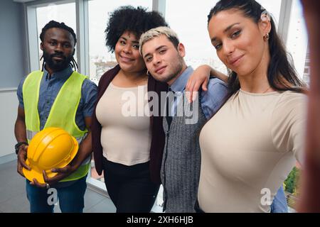 Selfie ritratto con telefono del gruppo di lavoro della società di consulenza che contrae lavori di ingegneria, due donne e due uomini, che posa guardando la macchina fotografica, uno dei Foto Stock