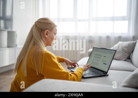 Una donna bionda lavora con molta attenzione dal suo ufficio domestico, scrivendo su un notebook Foto Stock
