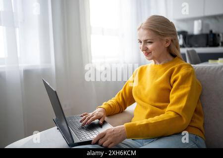 Una donna bionda lavora con molta attenzione dal suo ufficio domestico, scrivendo su un notebook Foto Stock