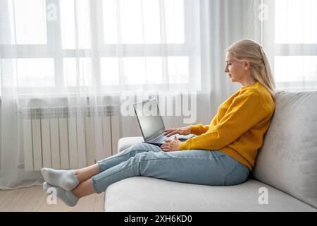 Una donna bionda lavora con molta attenzione dal suo ufficio domestico, scrivendo su un notebook Foto Stock