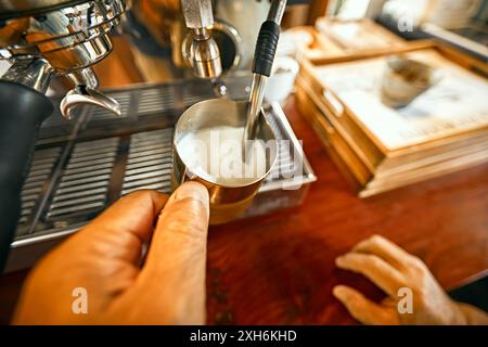 Primo piano, il barista prepara la schiuma di latte caldo su una macchina per il caffè Foto Stock