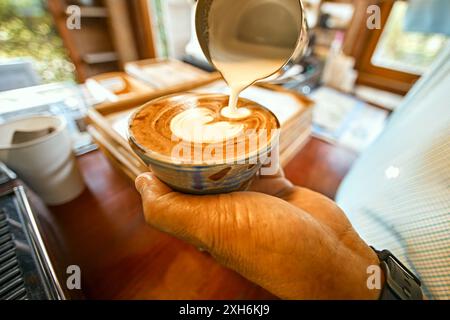 Primo piano della latte art di caffè versata a mano. Barista che versa latte Art Foto Stock