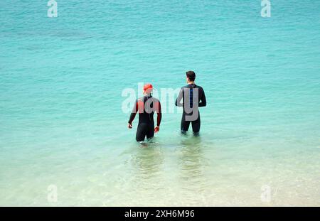 Due nuotatori maschili in muta con vista sul mare in piena luce del sole. Foto Stock