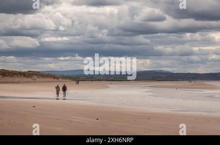 05.22.2021, Aberlady, Scozia: Una coppia che cammina sulla spiaggia della riserva naturale di Aberlady in una giornata nuvolosa con più persone sullo sfondo Foto Stock