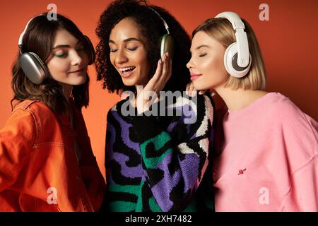 Tre giovani donne, vestite con abiti vivaci, indossano le cuffie e condividono un momento di connessione e comunicazione mentre si guardano l'un l'altra. Foto Stock