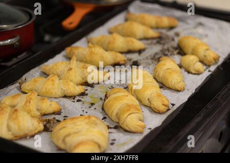 Un primo piano di croissant appena sfornati su un vassoio da forno con carta pergamena in cucina Foto Stock