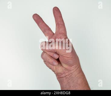 Mano maschile caucasica con pollice e due dita separate su sfondo bianco che indicano il numero due o il segno di vittoria o di pace Foto Stock