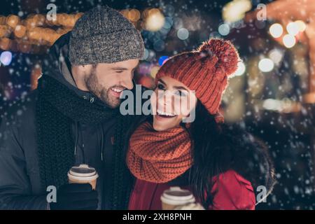 Foto di due persone divertenti coppia con bevanda calda nelle mani di spendere X-mas sera insieme avendo miglior tempo libero indossa cappotti caldo a maglia e tappi Foto Stock