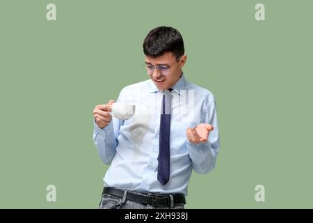 Giovane stressato con macchie di caffè sulla camicia su sfondo verde Foto Stock