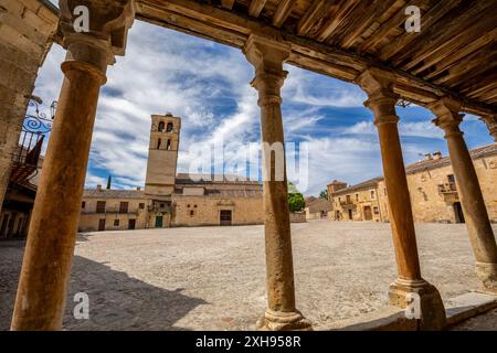 Vista dalle arcate di un antico edificio nella Plaza Mayor di Pedraza, Segovia, Castilla y Leon, Spagna, con la chiesa sullo sfondo Foto Stock