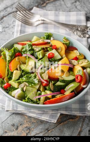 Insalata di avocado di pesca con cipolla, peperoncino, rucola, spinaci e semi di zucca da vicino in un recipiente sul tavolo. Verticale Foto Stock