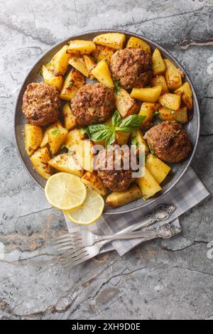 Polpette di manzo greche Bifteki con spicchi di patate in una salsa di olio d'oliva al limone primo piano sul piatto del tavolo. Vista dall'alto verticale Foto Stock