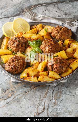 Polpette di manzo greche Bifteki con spicchi di patate in una salsa di olio d'oliva al limone primo piano sul piatto del tavolo. Verticale Foto Stock