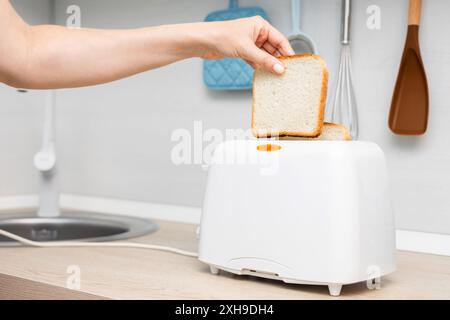 mano di donna che mette il pane nel tostapane. casalinga che frigge il pane in un tostapane, in cucina. donna che fa un brindisi. tostare il pane in un tostapane. Foto Stock