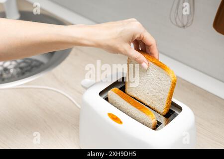 mano di donna che mette il pane nel tostapane. casalinga che frigge il pane in un tostapane, in cucina. donna che fa un brindisi. tostare il pane in un tostapane. Foto Stock