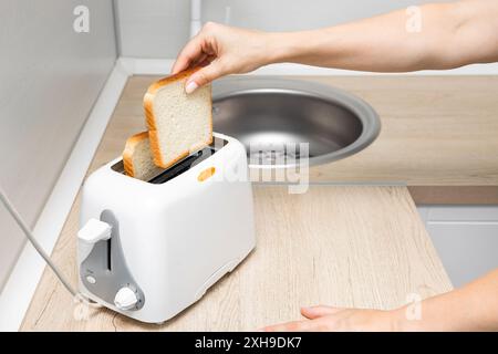 mano di donna che mette il pane nel tostapane. casalinga che frigge il pane in un tostapane, in cucina. donna che fa un brindisi. tostare il pane in un tostapane. classi Foto Stock