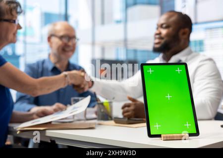 Il consulente finanziario stringe la mano agli anziani dopo aver scelto un piano pensionistico per assicurarsi la pensione, tablet con schermo verde. Banchiere che parla con una coppia di anziani dell'assicurazione sulla vita. Foto Stock