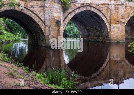 Una vista panoramica del fiume Tees a Yarm che mostra il ponte stradale e le rive alberate del fiume con riflessi sull'acqua Foto Stock