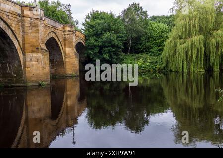 Una vista panoramica del fiume Tees a Yarm che mostra il ponte stradale e le rive alberate del fiume con riflessi sull'acqua Foto Stock