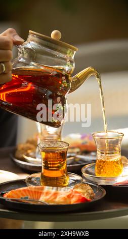 Versare il tradizionale tè persiano, servito con deliziosi dolci, perfetto per un pomeriggio rilassante Foto Stock