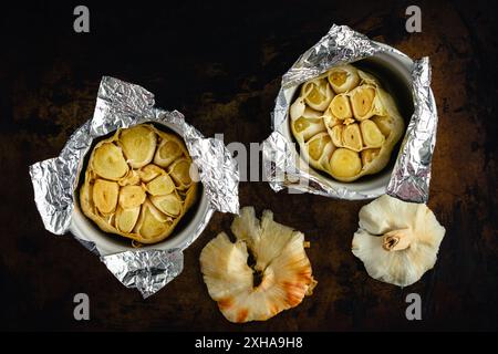 Bulbi di aglio arrosto in camamini ricoperti di Foil: Due teste di aglio che sono state arrostite in olio d'oliva all'interno di piccole ciotole di ceramica Foto Stock