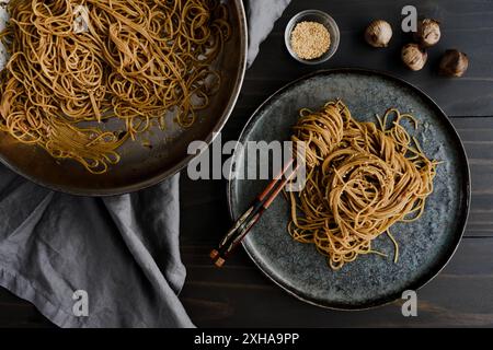 Tagliatelle di sesamo all'aglio nero servite su un piatto: Bacchette avvolte in tagliatelle e salsa di aglio e sesamo arrosto su un piatto con una padella a lato Foto Stock
