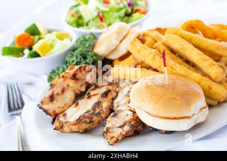 Vista di una cena a base di pollo, con panini, patate fritte e anelli di cipolla. Foto Stock