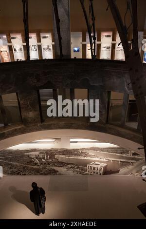 Un turista del museo dei bombardamenti atomici guarda le immagini del bombardamento sotto una replica in scala della famosa cupola A bomba. Hiroshima, giappone Foto Stock