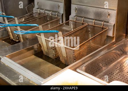 Vista di una fila di cesti vuoti appesi a un apparecchio per friggere, in un ambiente della cucina del ristorante. Foto Stock