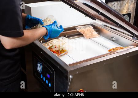 Vista di una persona che prepara sacchetti per alimenti sigillati in plastica nell'apparecchio sigillante per camera sottovuoto. Foto Stock