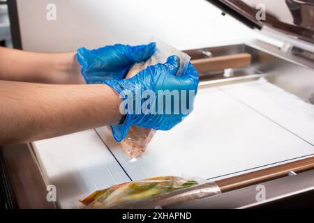 Un'immagine di una persona che utilizza una macchina per imballaggio sottovuoto, utilizzata nel settore per sigillare sacchetti di plastica di alimenti. I sacchetti di preparazione dei pasti sono in fase di preparazione. Foto Stock