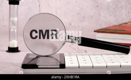 Concetto di relazione gestita dal cliente. Parola CMR attraverso una lente di ingrandimento su una parete grigia, vista frontale Foto Stock