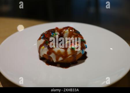 Ciambella con salsa al cioccolato e spruzzi colorati su un piatto bianco Foto Stock